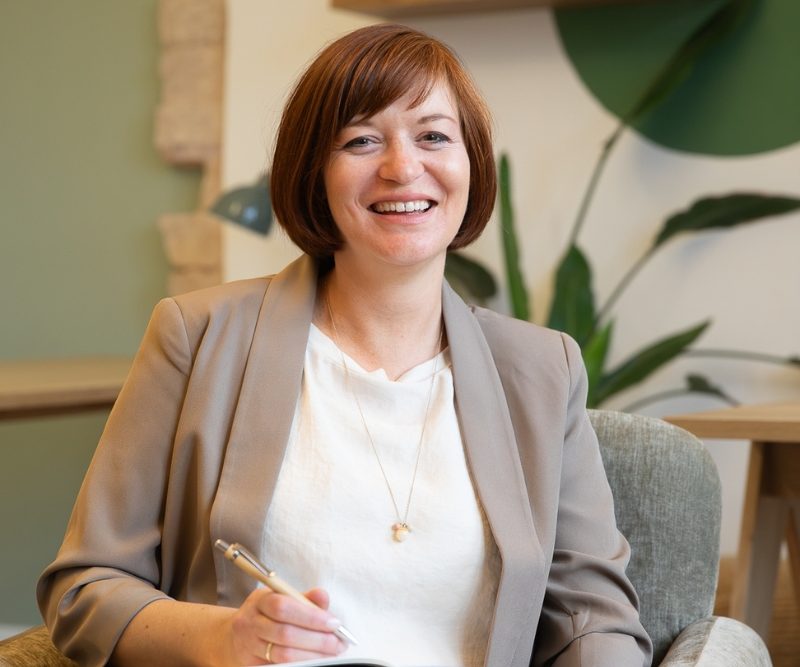 Birgit Gebauer, lächelnd, sitzt in einem modernen Büro.