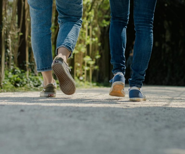 Zwei Personen gehen auf einem Waldweg, Rückenansicht, in bequemen Schuhen, Walk & Talk