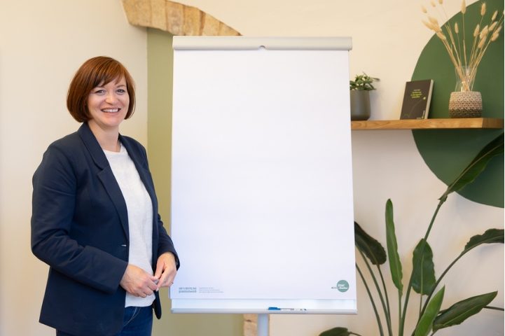 Porträtfoto Birgit Gebauer (Eva Korn) Birgit Gebauer steht lächelnd neben einem Flipchart, Führung, Nachwuchsführungskraft