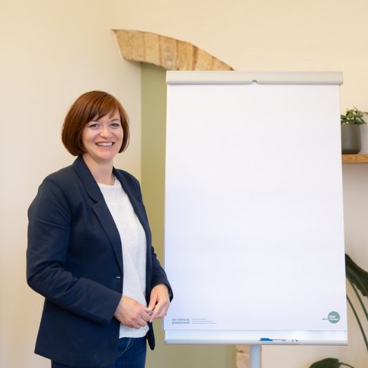 Birgit Gebauer steht neben einem Flipchart in einem hellen Raum.