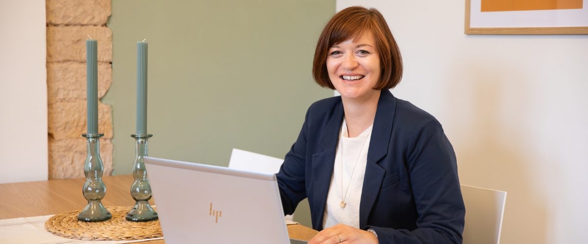 Birgit Gebauer lächelt am Schreibtisch neben zwei Kerzenständern, Portrait