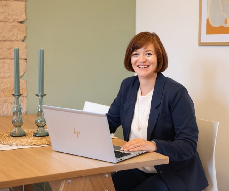 Birgit Gebauer sitzt am Tisch mit Laptop und Notizbuch in modernem Büro, Online-Coaching