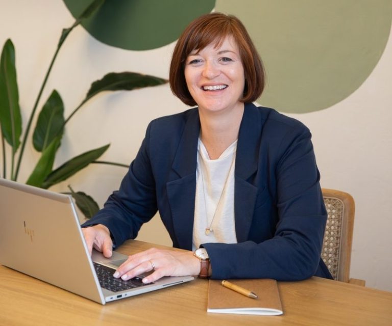 Birgit Gebauer sitzt am Tisch mit Laptop und Notizbuch in modernem Büro, Online-Coaching