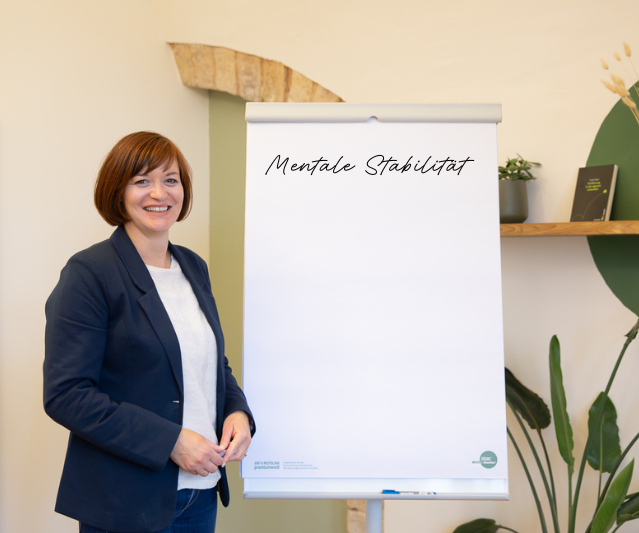 Birgit in einem blauen Blazer, lächelt in einem modernen Büro.